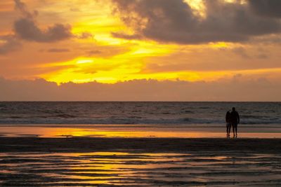 Silhouette people standing on beach against sky during sunset