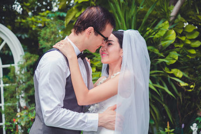 Bride and groom embracing against trees