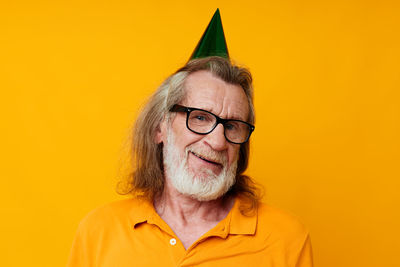 Portrait of senior man wearing party hat against yellow background