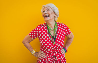 Smiling senior woman standing against yellow background