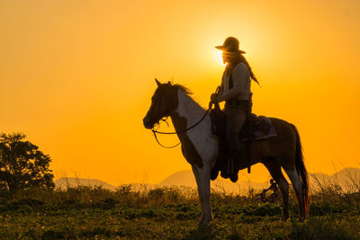 Man riding horse on field during sunset