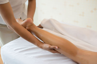 Midsection of masseur massaging leg of woman on table in spa