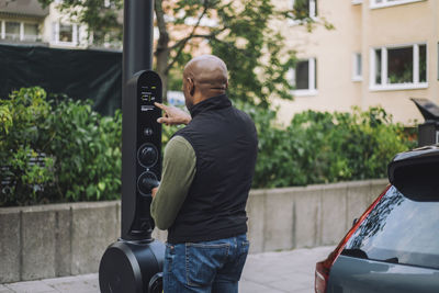 Mature man operating kiosk while charging car at station