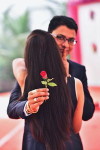 Portrait of bridegroom holding rose while embracing bride