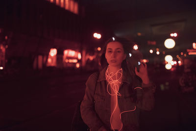 Portrait of young woman standing on road at night