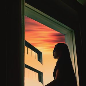 Portrait of young woman looking through window at sunset