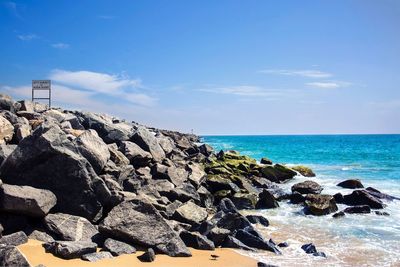 Rocks on shore by sea against blue sky