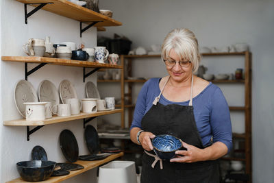 Potter artist showing her work in studio. mature ceramist standing at workshop with clay cups in