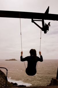 Rear view of woman sitting on swing against sea