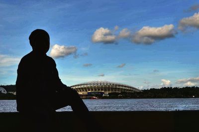 Silhouette man on bridge over river against sky in city