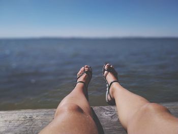 Low section of woman relaxing on pier over sea
