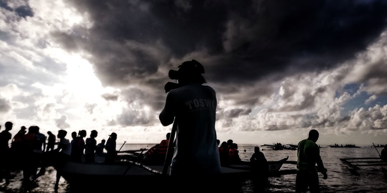 GROUP OF PEOPLE AT SEA AGAINST SKY