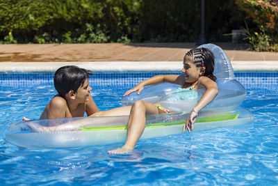 Two children on an inflatable mat in a swimming pool