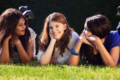 Smiling friends lying on field in park