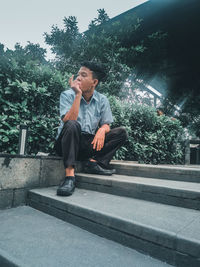 Young man looking away while sitting on tree