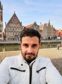 Portrait of man standing on walkway against buildings in city