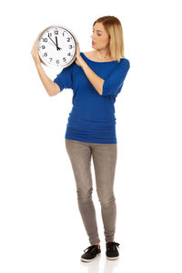 Young woman holding wall clock against white background
