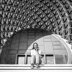 Portrait of smiling woman sitting against modern building