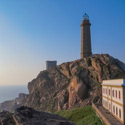 Lighthouse by sea against buildings against clear sky