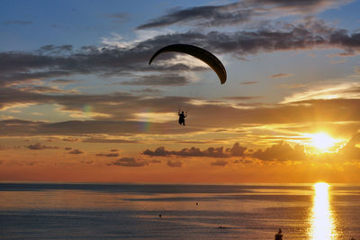 Silhouette paragilider over sea against sky during sunset