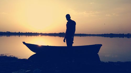 Silhouette man standing by lake against sky during sunset