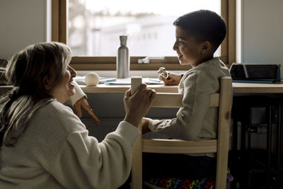 Smiling son talking with mother while sitting on chair at home