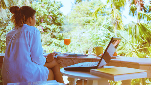 Rear view of woman using phone while sitting on table