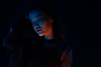 Portrait of young woman looking away against black background