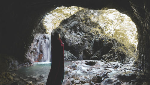 Woman standing on rock against waterfall 