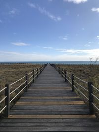 View of wooden footbridge leading towards sea against sky