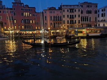 Boats in canal by buildings in city at night
