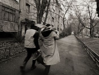 Rear view of people walking on road along bare trees