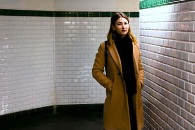 Young woman looking away while standing against wall