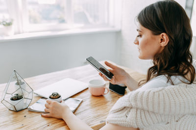 Young woman using mobile phone on table