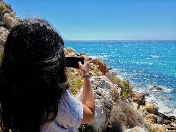 Rear view of woman photographing sea against sky