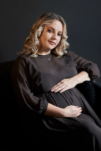 Portrait of beautiful young woman sitting against black background