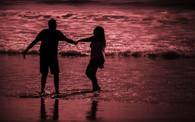 Silhouette couple standing on beach against sky during sunset