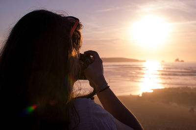 Rear view of woman at beach during sunset making a photograph