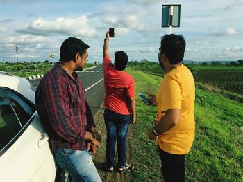 Friends taking selfie through mobile phone while standing on roadside