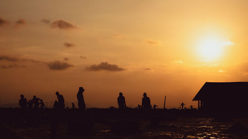 Silhouette people on beach against sky during sunset