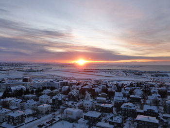 Snow covered townscape against sky during sunset