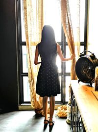 Rear view of woman looking through window at home