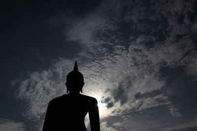 Low angle view of silhouette buddha statue against sky