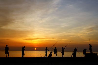 Silhouette people playing on beach against sky during sunset