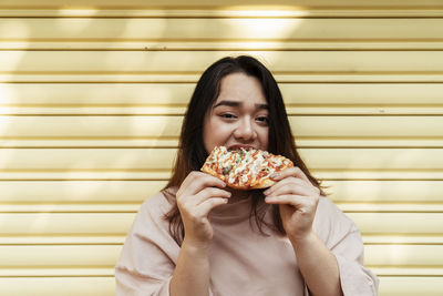 Portrait of smiling young woman eating food against wall