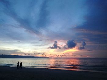 Silhouette people at beach against cloudy sky during sunset