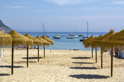 Straw parasols on a sandy beach with a yachts sailing on the background