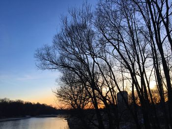 Silhouette bare trees by lake against sky during sunset