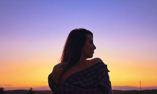 Young woman looking away against sky during sunset