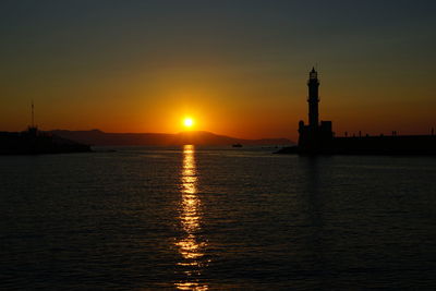 Silhouette of lighthouse sailing on sea during sunset